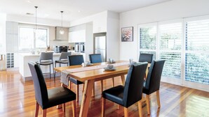A modern kitchen with white cabinets, a wooden dining table, and black chairs. - Modern Holiday House wth Bay View (Frankston South)