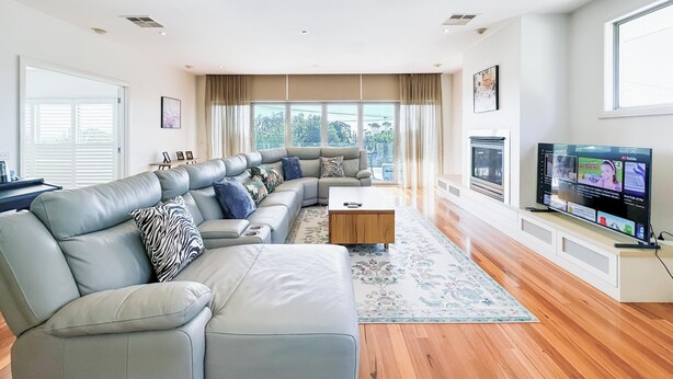 A modern living room with a sectional sofa, a coffee table, and a TV. - Modern Holiday House wth Bay View (Frankston South)