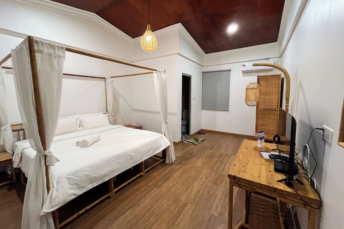 A room with a four-poster bed, a wooden desk with a computer, and a ceiling light fixture.