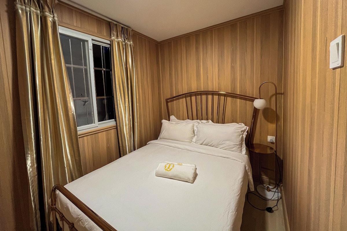 A single bed with a headboard, a bedside lamp, and a window with curtains.