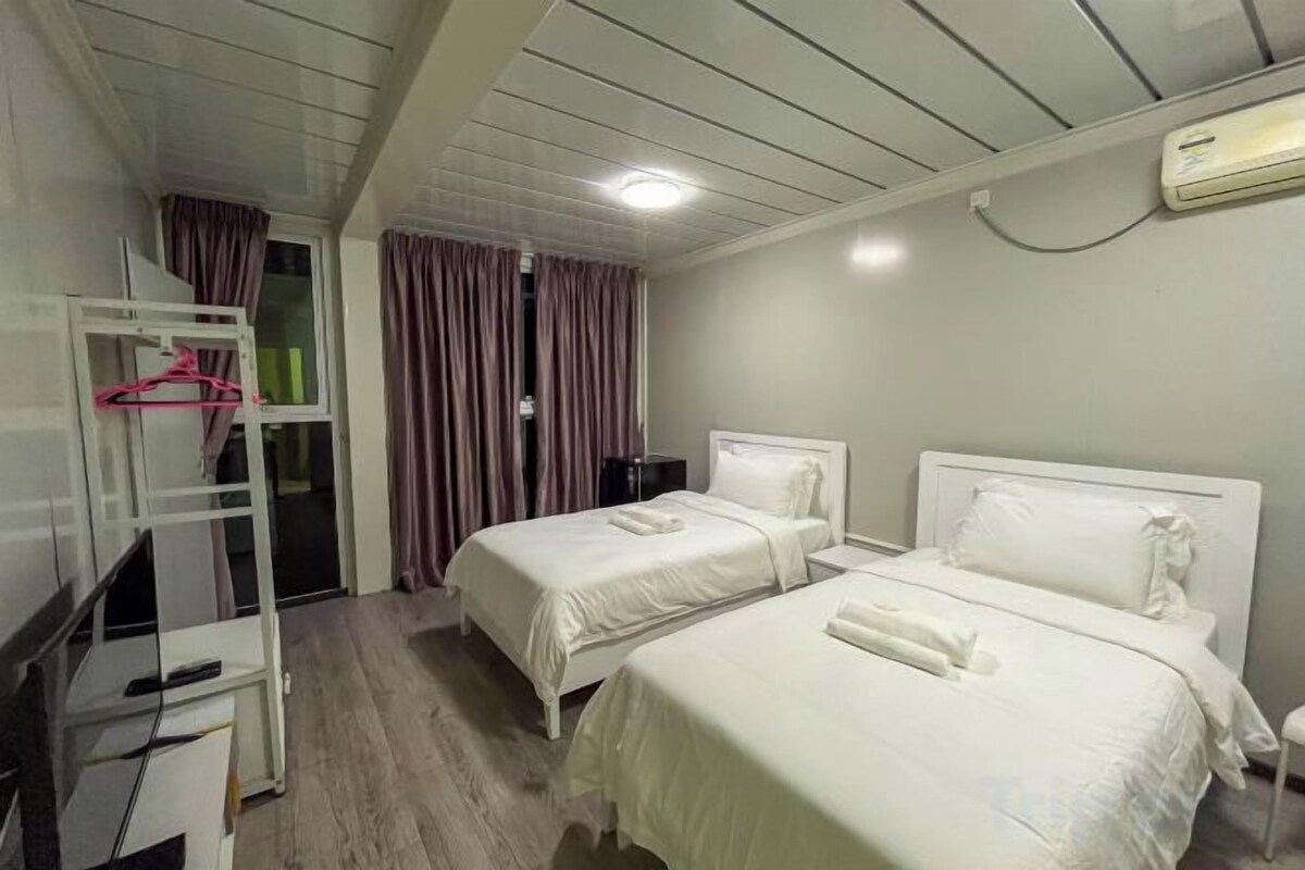 A hotel room with two beds, a desk with a chair, a TV, and a wardrobe.