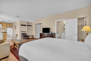 Une chambre d’hôtel avec un grand lit, un bureau, une chaise, une télévision et une salle de bain visible à travers une porte ouverte.