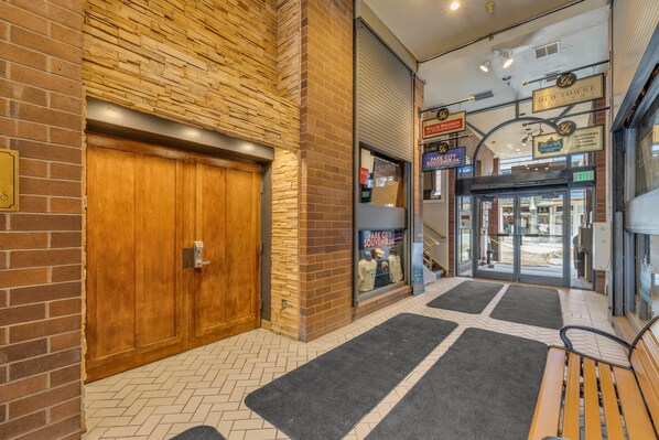 Un couloir avec une porte en bois, un mur en pierre et une porte en verre donnant sur un magasin.