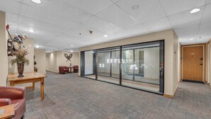 Un vestíbulo espacioso con un mostrador de recepción de madera, una zona de estar con sillones de cuero y un muro divisorio de vidrio.