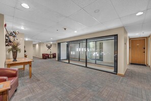 Un hall d’entrée spacieux avec un comptoir de réception en bois, un coin salon avec des fauteuils en cuir et une cloison en verre.