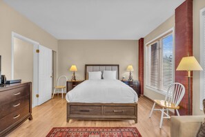 Un dormitorio con cama, mesitas de noche, cómoda, silla y ventana con persianas.