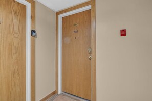 Una puerta de madera con una placa de número, un timbre y un detector de incendios en la pared.