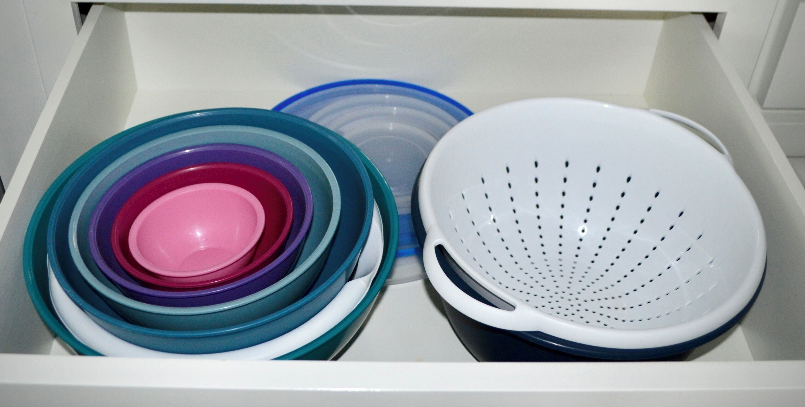 A drawer containing stacked plastic containers and a white colander.