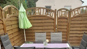 A patio with a table and chairs, a wooden fence, and a house in the background.