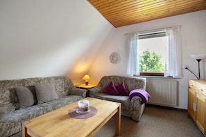 Une chambre meublée avec un canapé, une table avec une tasse, une lampe, un radiateur et une fenêtre donnant sur un paysage agréable.
