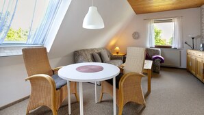 Een kamer met een ronde tafel, rieten stoelen, een bank, een lamp en een raam met gordijnen.