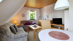 Een woonkamer met een bank, een tafel, een lamp, een televisie en een plafond met houten balken.
