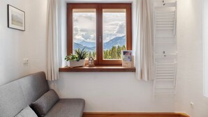 Una habitación con ventana, un sofá, una mesita con una planta y un tendedero blanco.