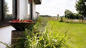 A white building with a window, a black planter with red flowers, and a grassy area with a fence in the background. - Apartment 'Balkonwohnung' with Shared Garden, Balcony and Wi-Fi (Westerdeichstrich)