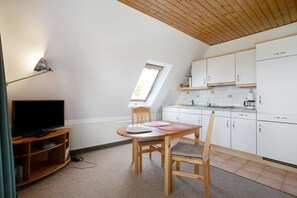A compact kitchen with white cabinets, a wooden dining table, and a television on a stand.