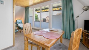A room with a wooden ceiling, a dining table with two placemats, a television, and a chair with a cushion. - Apartment 'Balkonwohnung' with Shared Garden, Balcony and Wi-Fi (Westerdeichstrich)