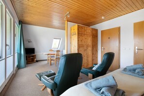 A room with a bed, two reclining chairs, a wooden wardrobe, a television, and a desk with a chair.