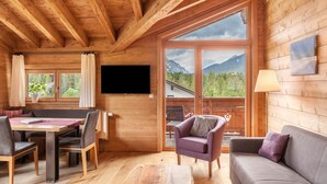 A wooden cabin interior with a dining area, a sofa, and a large window with a mountain view. - 'Blockhaus Sonnenspitz' holiday flat with mountain views, communal garden and WLAN (Leutasch)