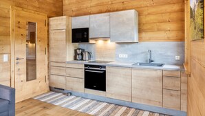 A compact kitchen with wooden walls, a built-in oven, a microwave, and a sink. - 'Blockhaus Sonnenspitz' holiday flat with mountain views, communal garden and WLAN (Leutasch)