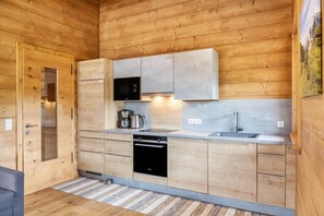 A compact kitchen with wooden walls, a built-in oven, a microwave, and a sink.