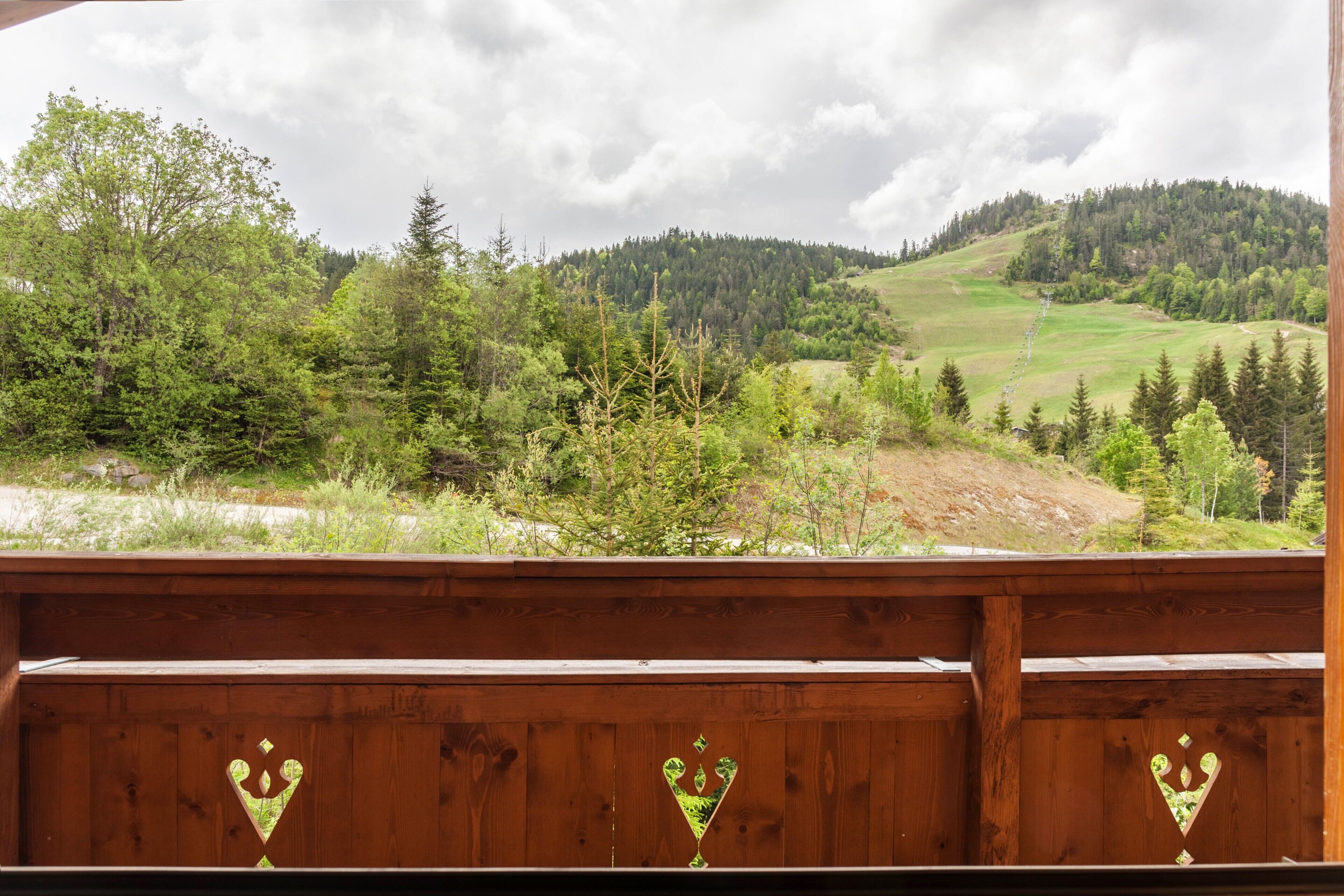 Una terraza de madera con formas de corazón, con vistas a un valle boscoso y una colina distante.