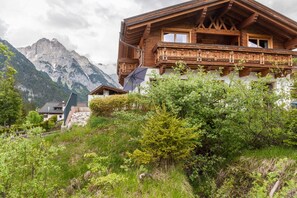 Un chalet en bois doté d’un balcon, entouré d’une végétation luxuriante et avec des montagnes en toile de fond.