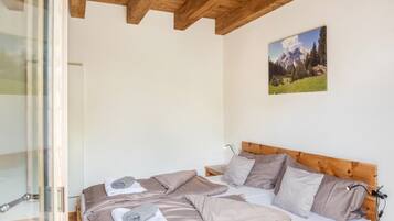 A bedroom with a wooden ceiling, a bed with multiple pillows, a nightstand, and a painting of a mountain landscape.