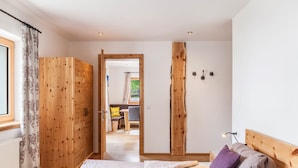 Ein Schlafzimmer mit einem Holzschrank, einem Bett mit Kissen, einer Holz Kopfteil und Blick in einen weiteren Raum.