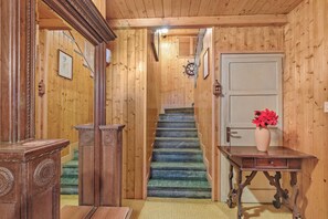 Interior de madera con una escalera, una puerta y una mesa con un florero.