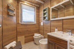 A compact bathroom with wooden paneling, a toilet, a sink with a mirror, and a small window. - La Lanterna: Hillside Lake Maggiore Stay With Pool (Gignese)