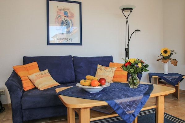 A living room with a sofa, a coffee table with fruit, a vase with flowers, and a lamp.