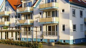 A multi-story hotel with balconies, a sign reading 'RESIDENZ AM STRAND', and a paved entrance area.
