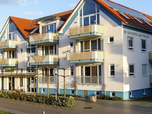 A multi-story hotel with balconies, a sign reading 'RESIDENZ AM STRAND', and a paved entrance area.