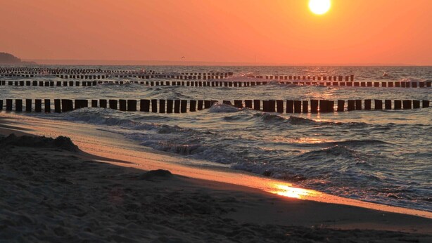 A beach with waves, a sunset, and a pier.