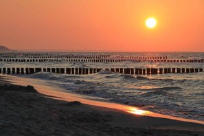 A beach with waves, a sunset, and a pier.