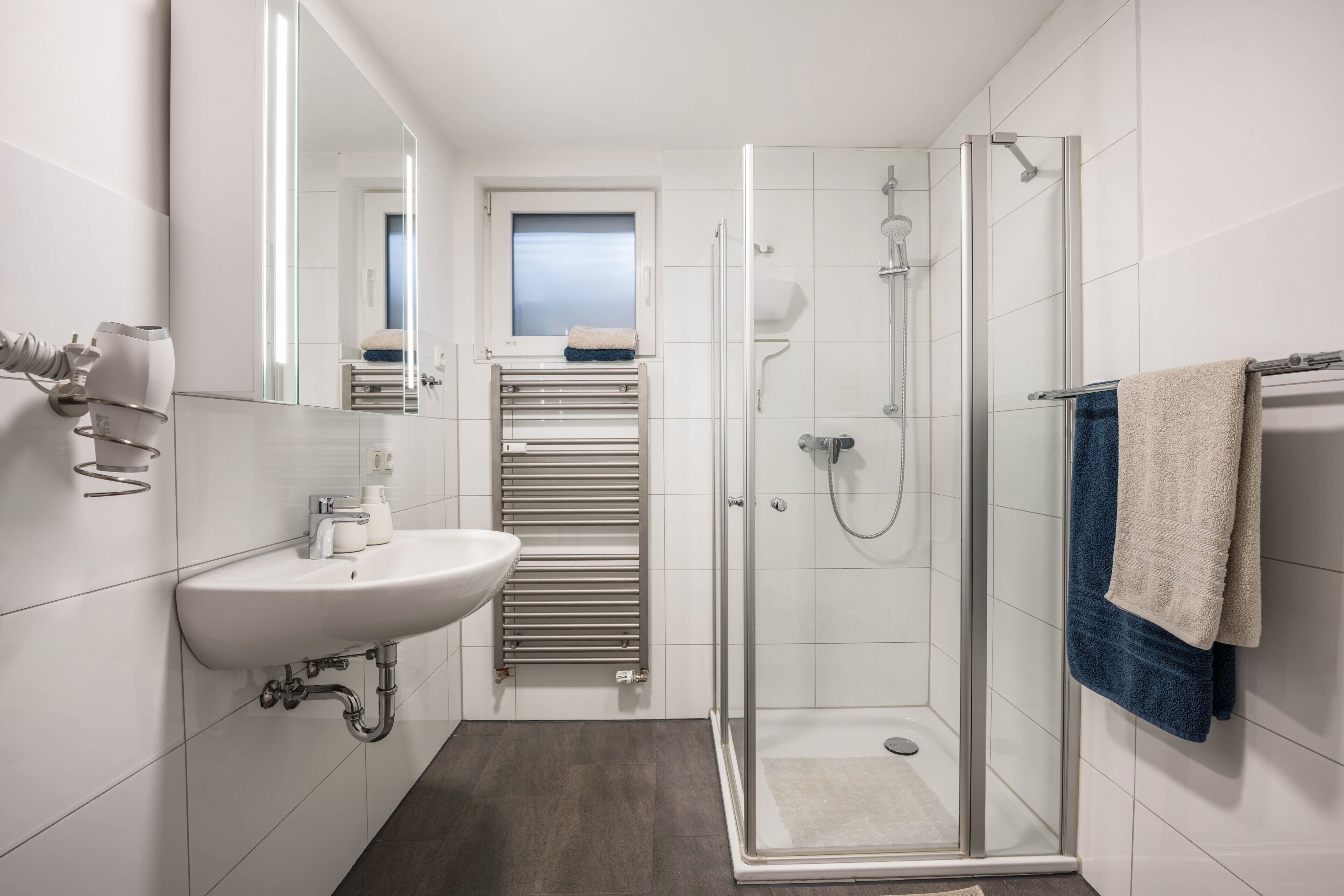 Een moderne badkamer met een glazen douchecabine, een wastafel met een handdoekhouder en een raam boven de spiegel.