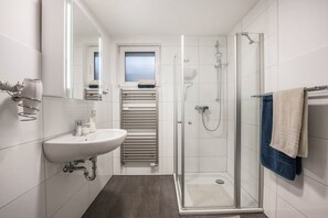 A modern bathroom with a glass shower enclosure, a sink with a towel rack, and a window above the mirror.