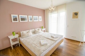 A bedroom with a large bed, bedside tables, a chandelier, framed pictures on the wall, and a window with curtains. - Apartment 'Bianca's Kaiserstuhl' with Private Terrace, Balcony and Wi-Fi (Ihringen)