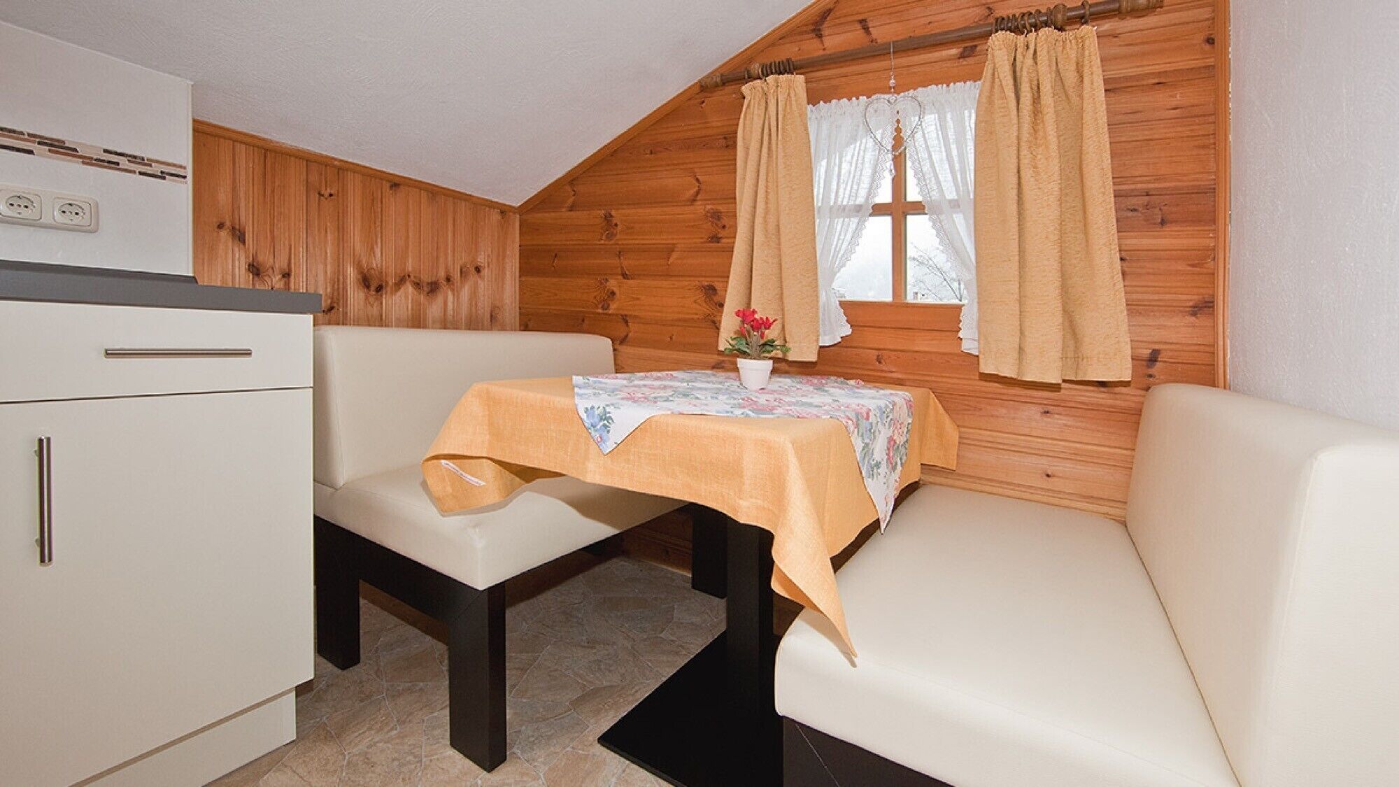 Eine kleine Küchenzeile mit Kühlschrank, einem weißen Schrank und einem Tisch mit Blumenmuster.