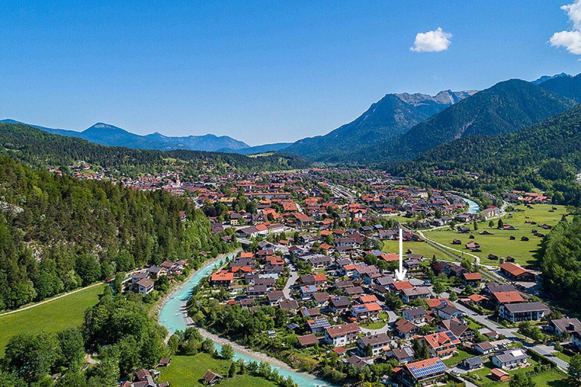 Eine Stadt mit einem Fluss, umgeben von Bergen, mit roten Dächern und grünen Landschaften.