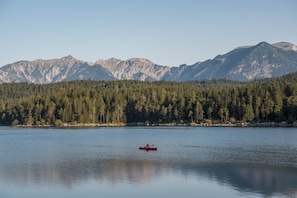A calm lake with a red kayak, surrounded by dense forest and mountains in the background.