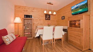 Un'accogliente stanza con un divano rosso, un tavolo da pranzo con sedie, una TV, una libreria e un mobiletto in legno.
