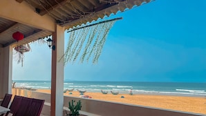 A beach view from a covered area with chairs and a potted plant. - Jeju Beach Front Villa (Da Nang)