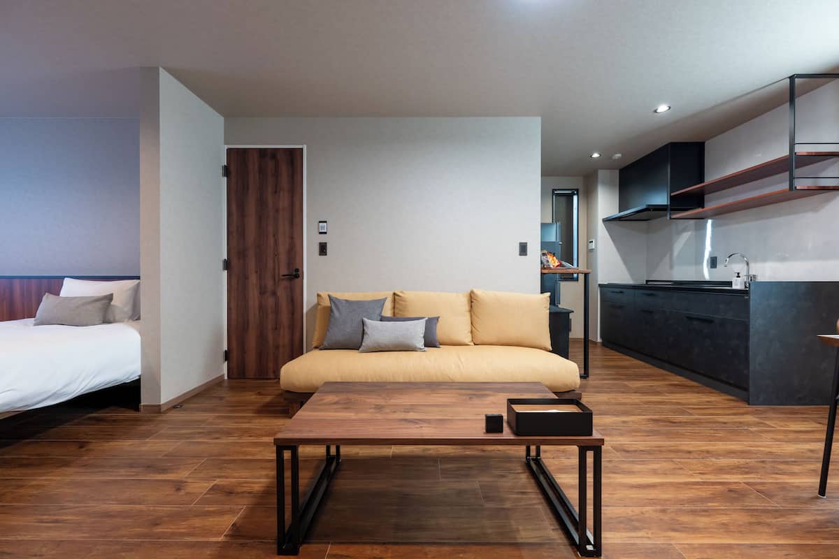 Una habitación de hotel moderna con sofá, una mesa de centro de madera, cama y kitchenette.