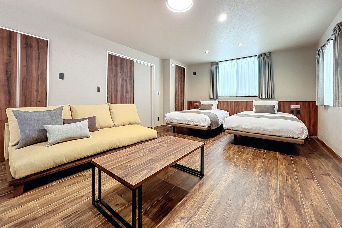 Una habitación de hotel moderna con suelo de madera, un sofá, una cama y una mesita.