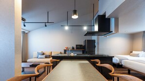Una habitación de hotel moderna con zona de comedor, sofá, cama y kitchenette.