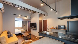 Habitación de hotel moderna con sofá, una mesa de comedor, una zona de cocina con fregadero y un televisor.