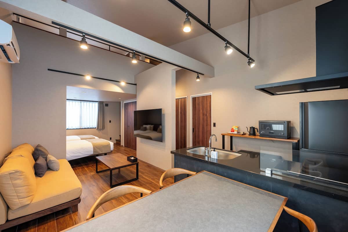 Habitación de hotel moderna con sofá, una mesa de comedor, una zona de cocina con fregadero y un televisor.