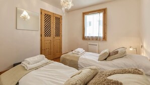 Un dormitorio con dos camas, un armario de madera, una ventana con cortinas y una lámpara colgante.