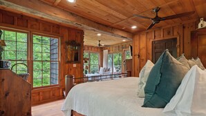 A wooden cabin bedroom with a large bed, multiple windows, and a ceiling fan.